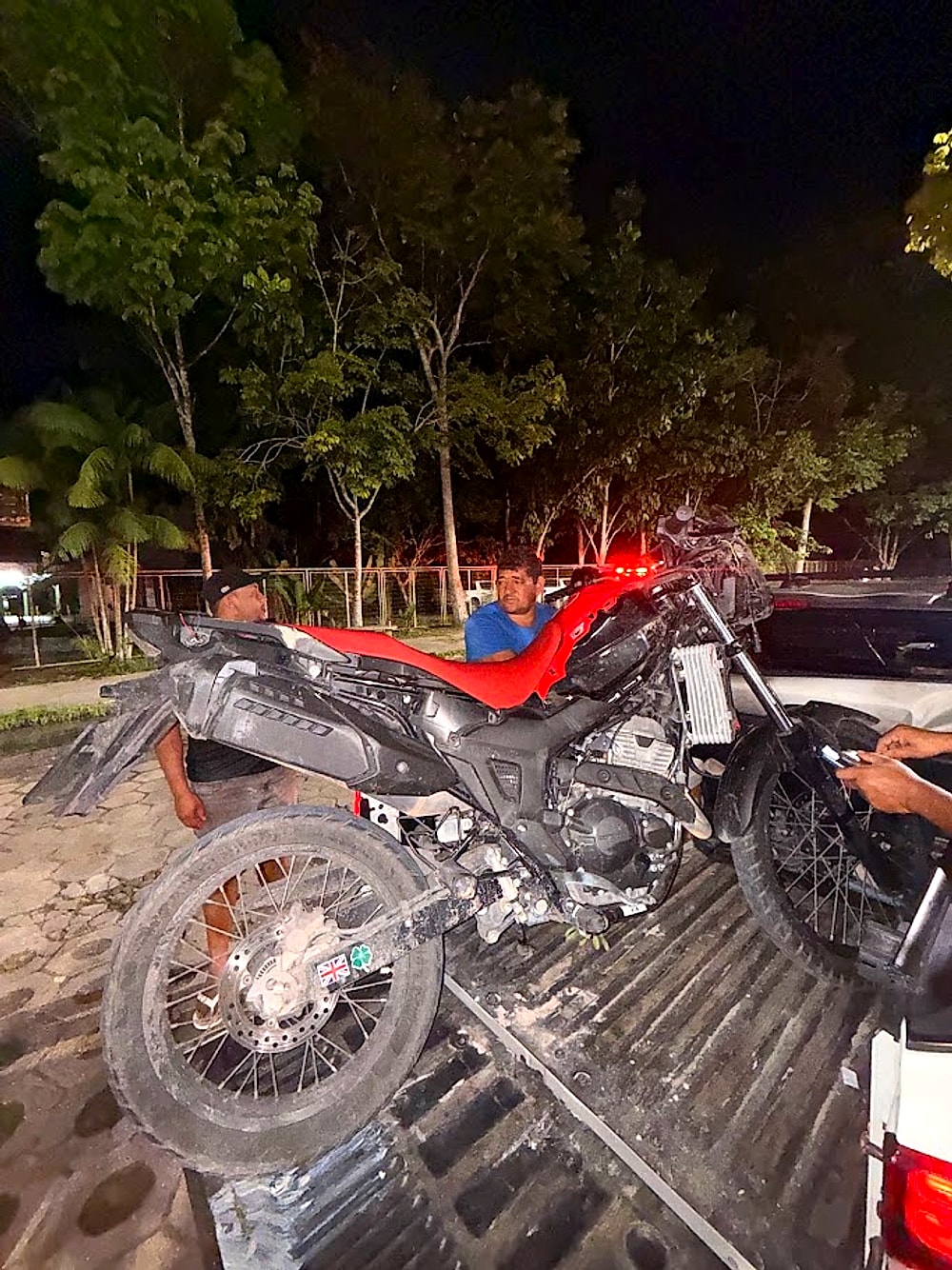 Moto trail vermelha recuperada e carregada na caminhonete da equipe de resgate à noite